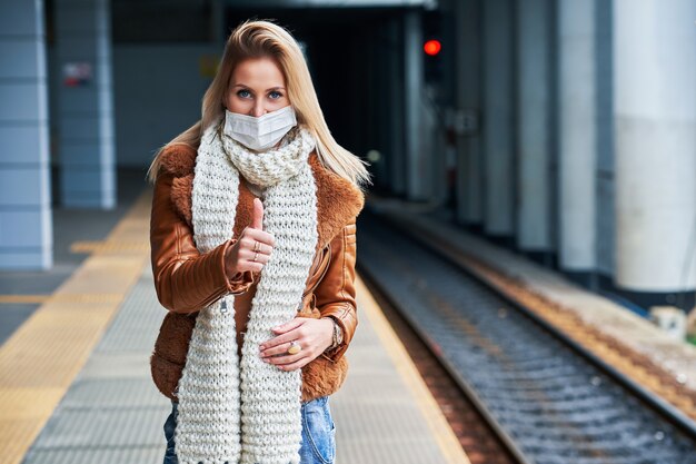 donna adulta alla stazione ferroviaria che indossa maschere a causa delle restrizioni covid-19