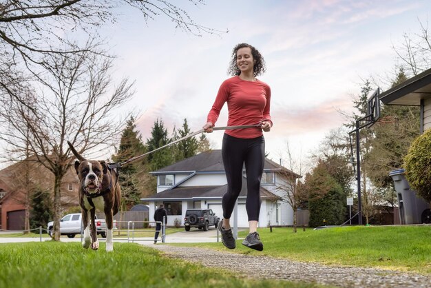 Donna adulta caucasica atletica che corre fuori con un cane boxer