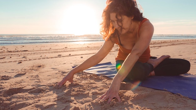 Donna adulta che fa un esercizio di stretching su una stuoia sulla spiaggia