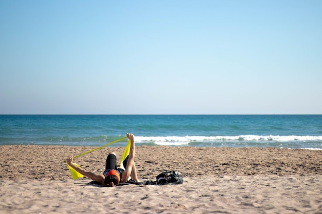 Donna adulta che si esercita con gli elastici sulla spiaggia sdraiata sulla spiaggia