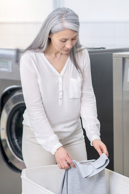 Donna adulta con i capelli lunghi in abiti bianchi, guardando da vicino il colletto della maglietta grigia lavata al lavaggio a secco