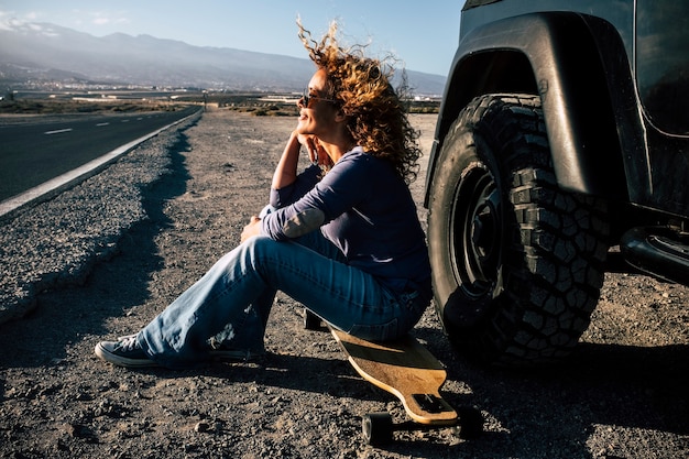 Donna adulta con un longboard fuori dall'auto con una lunga strada sullo sfondo in