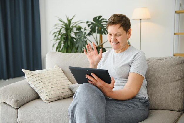 Donna adulta di mezza età matura che tiene una conferenza di computer con tablet digitale chiamata da una riunione di chat online di famiglia virtuale a distanza sociale