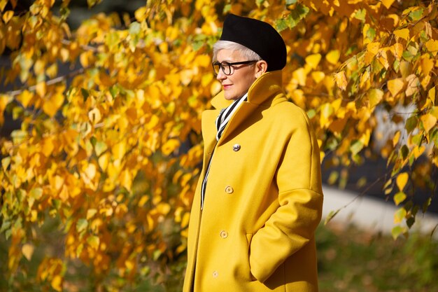 donna adulta in cappotto giallo nel parco in autunno