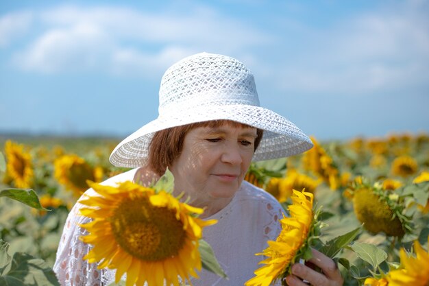 Donna adulta in un cappello bianco in un campo di girasoli