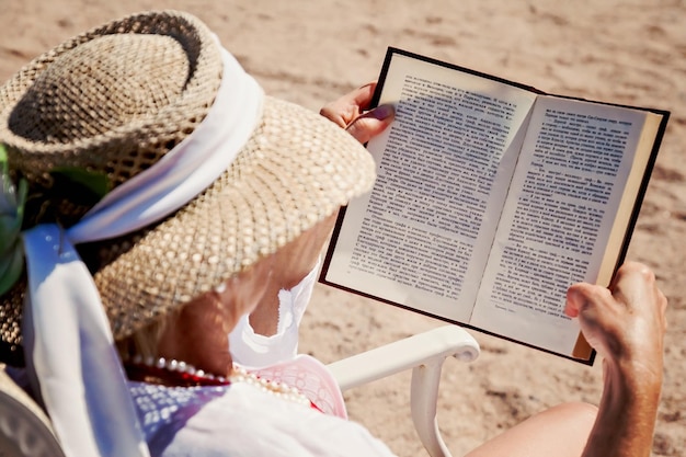 Donna adulta in un cappello su una spiaggia che legge un libro stampato