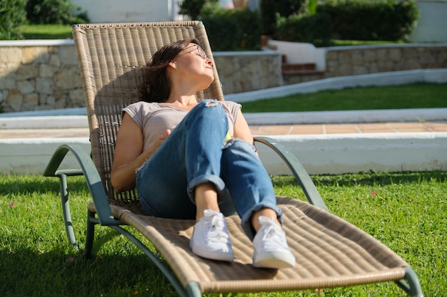 Donna adulta matura che riposa sdraiata su una sedia all'aperto sul prato. Riposo, relax, stile di vita, vacanza, persone di mezza età