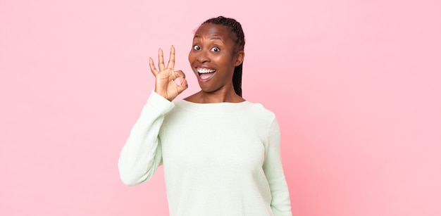 Donna adulta nera afro che si sente di successo e soddisfatta, sorride con la bocca spalancata, fa un segno ok con la mano