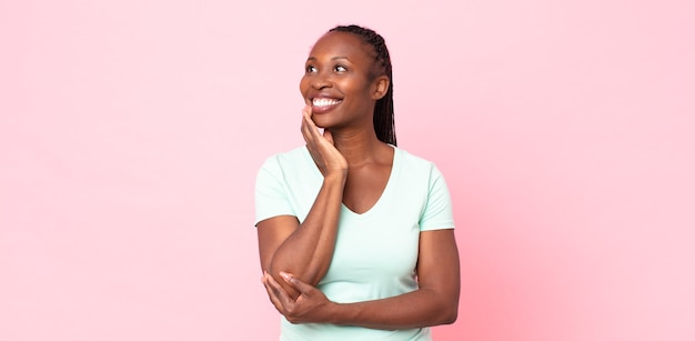 Donna adulta nera afro che sorride felicemente e sogna ad occhi aperti o dubita, guardando di lato