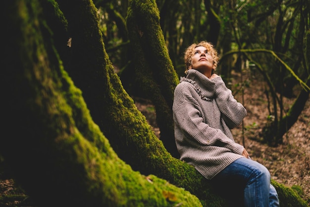 Donna adulta seduta su un tronco con muschio verde in una foresta tropicale di bellissimi boschi godendo di relax e connessione con la natura. Stile di vita delle persone dell'ambiente e dell'ambiente nel parco all'aperto