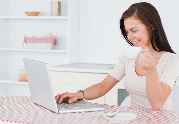 Donna affascinante che utilizza il suo computer portatile e che mangia un tè