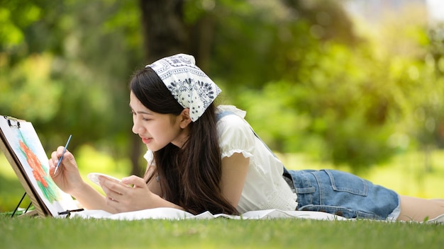 Donna affascinante della ragazza che si siede sul plaid al parco nella soleggiata giornata estiva e usando l'acquerello