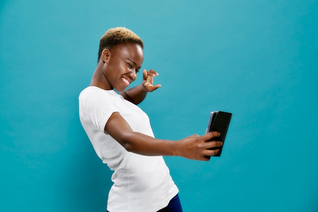 Donna africana allegra in camicia bianca che prende selfie