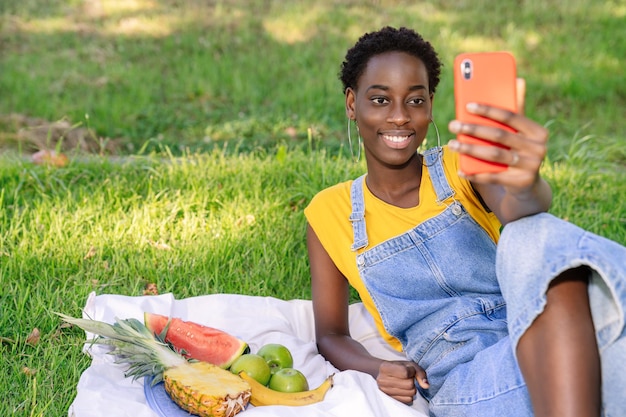 Donna africana che fa un selfie con il suo telefono cellulare mentre fa un picnic di frutta