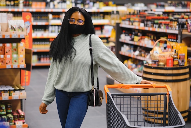 Donna africana che indossa una maschera medica usa e getta. Fare la spesa al supermercato durante l'epidemia di pandemia di coronavirus. Tempo di epidemia.