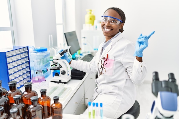 Donna africana che lavora al laboratorio dello scienziato sorridendo felice indicando con la mano e il dito di lato