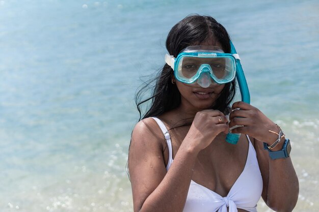 Donna africana con il corpo bagnato e guardando la fotocamera mentre si trova in mare e regola gli occhiali protettivi