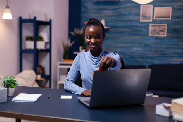 Donna africana creativa che mette note adesive sul computer portatile che lavora la sera per finire un progetto di lavoro. Libero professionista nero che rispetta la scadenza che studia a tarda notte.