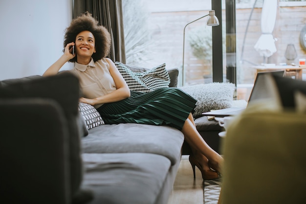 Donna africana dei giovani capelli ricci che si rilassa a casa e che per mezzo del telefono cellulare