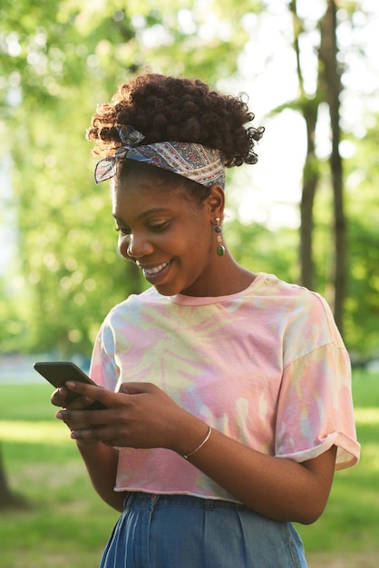 Donna africana felice che parla online usando il suo telefono cellulare mentre si trova nel parco