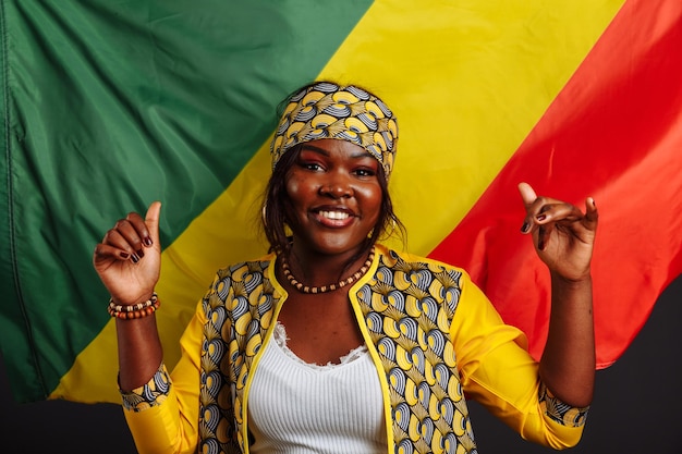 Donna africana in abiti nazionali che posano e ballano con i pollici in su contro la bandiera della repubblica del congo