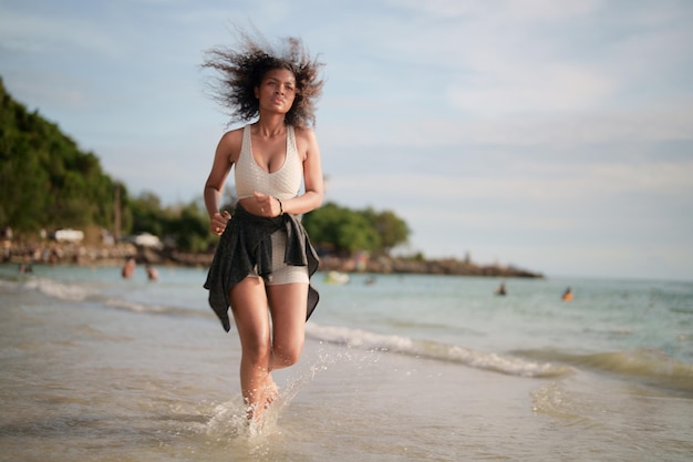 Donna africana in reggiseno sportivo è in esecuzione sulla spiaggia per l'allenamento all'aperto Ritratto sexy signora asiatica africana si prepara per il fitness in spiaggia