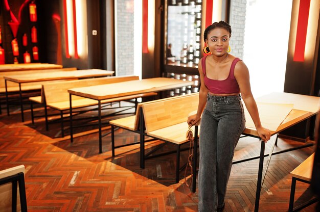 Donna africana in top rosso marsala e jeans in posa al coperto.