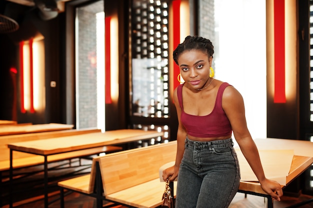 Donna africana in top rosso marsala e jeans in posa al coperto.