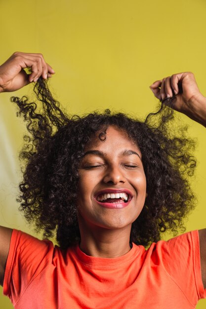 Donna afro-americana che sorride e gioca con i suoi capelli ricci su uno sfondo giallo.