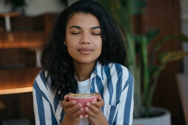 Donna afro-americana che tiene tazza di caffè, seduto in un caffè, concentrarsi sul viso