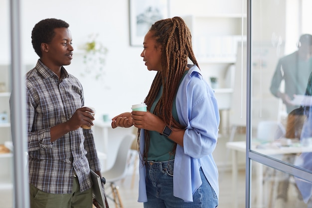 donna afro-americana contemporanea parlando al giovane collega durante la pausa caffè in ufficio