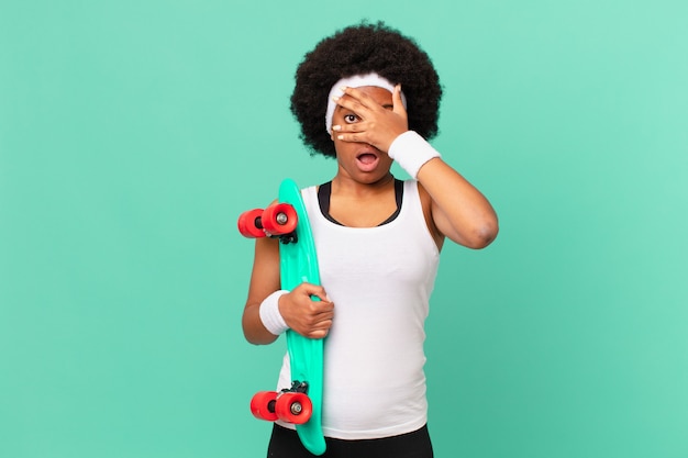 Donna afro che sembra scioccata, spaventata o terrorizzata, coprendo il viso con la mano e sbirciando tra le dita. concetto di skateboard