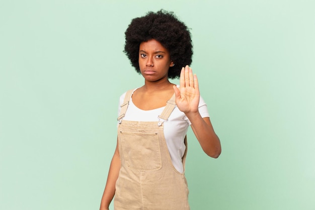 Donna afro che sembra seria, severa, dispiaciuta e arrabbiata che mostra il concetto di chef di gesto di stop facendo il palmo aperto