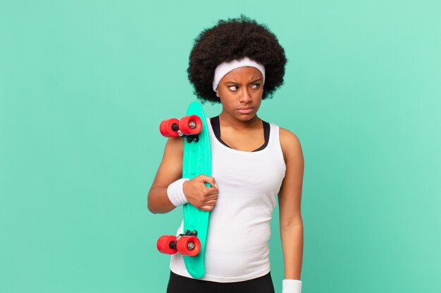 Donna afro che si sente triste, turbata o arrabbiata e guarda di lato con un atteggiamento negativo, accigliata in disaccordo. concetto di skateboard