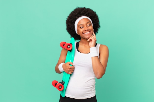 Donna afro che sorride felicemente e sogna ad occhi aperti o dubita, guardando di lato. concetto di skateboard