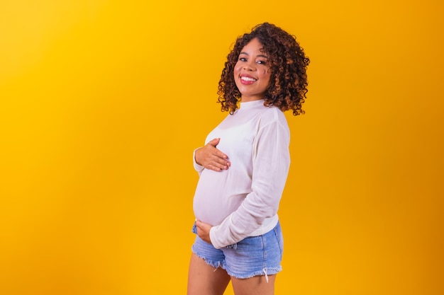 Donna afro incinta felice che tocca la sua pancia Ritratto di giovane madre incinta, accarezzandole il ventre e sorridendo in primo piano. concetto di gravidanza sana