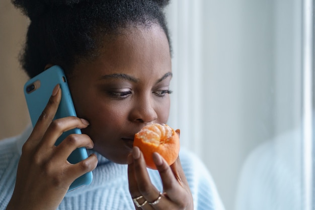 Donna afro malata che cerca di sentire l'odore di mezza arancia fresca di mandarino parlando al telefono. Covid-19