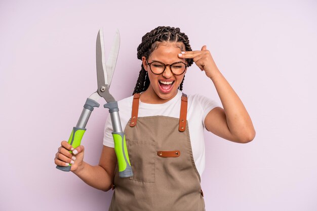 Donna afro nera che sembra infelice e stressata, gesto suicida che fa segno di pistola. concetto di giardiniere o agricoltore