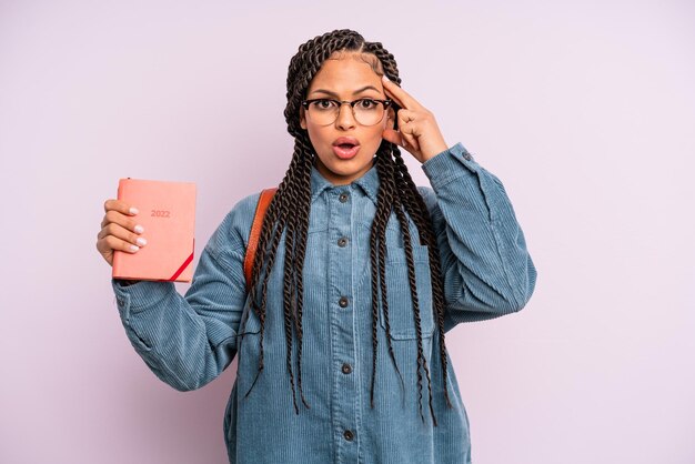 Donna afro nera che sembra sorpresa, realizzando un nuovo pensiero, idea o concetto. calendario degli studenti o concetto di agenda