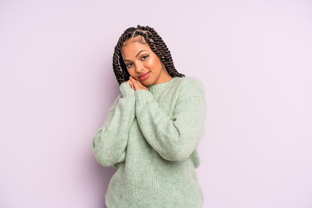 Donna afro nera che si sente innamorata e sembra carina, adorabile e felice, sorride romanticamente con le mani accanto al viso