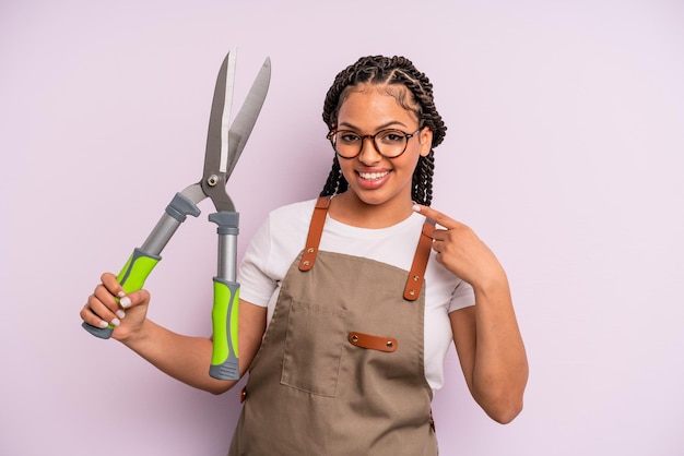 Donna afro nera che sorride con sicurezza indicando il proprio concetto di giardiniere o agricoltore con un sorriso ampio