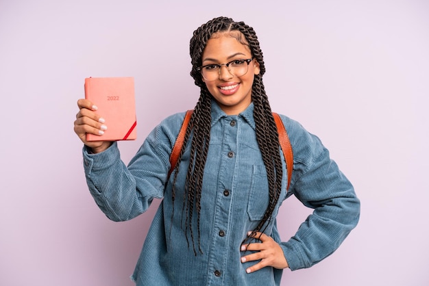 Donna afro nera che sorride felicemente con una mano sull'anca e sicura di sé. calendario degli studenti o concetto di agenda