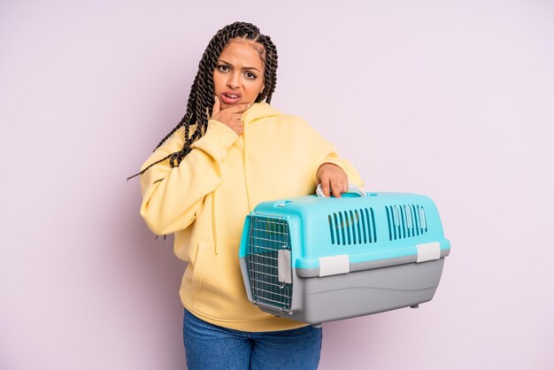 Donna afro nera con bocca e occhi spalancati e concetto di contenitore da viaggio per animali domestici con la mano sul mento