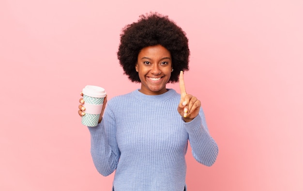 Donna afro sorridente e dall'aspetto amichevole, mostrando il numero uno o prima con la mano in avanti, conto alla rovescia. concetto di caffè