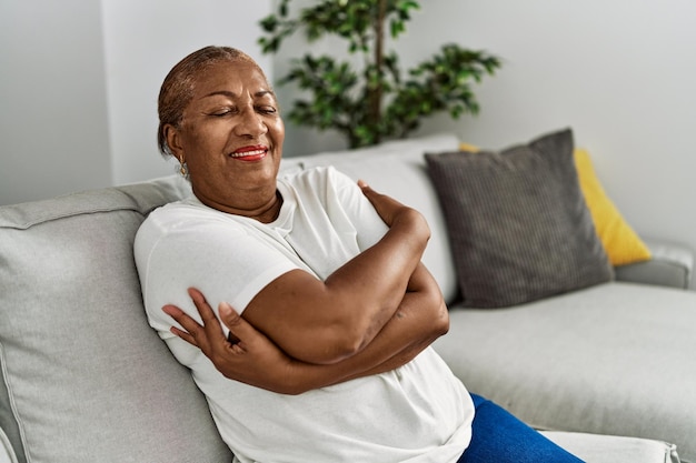 Donna afroamericana anziana che sorride fiduciosa abbracciandosi a casa