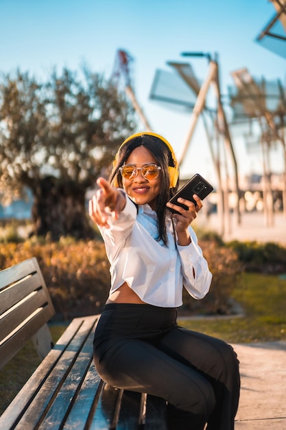 Donna afroamericana che ascolta musica con le cuffie al tramonto in un parco