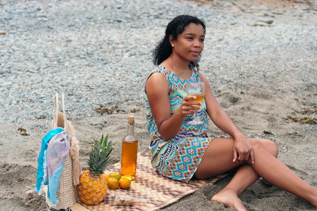 Donna afroamericana che beve un bicchiere di vino sulla spiaggia