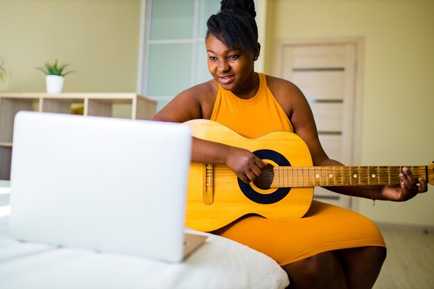 Donna afroamericana che gioca sulla chitarra wgile seduto in camera da letto
