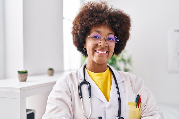 Donna afroamericana che indossa l'uniforme del medico sorridente fiducioso in piedi in clinica