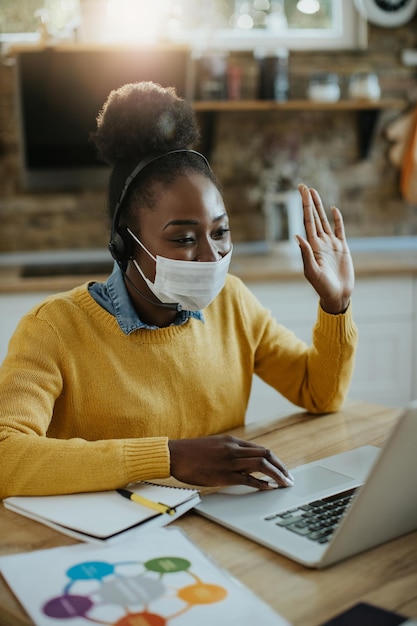 Donna afroamericana che saluta mentre tiene una riunione di lavoro online a casa a causa della pandemia di COVID19